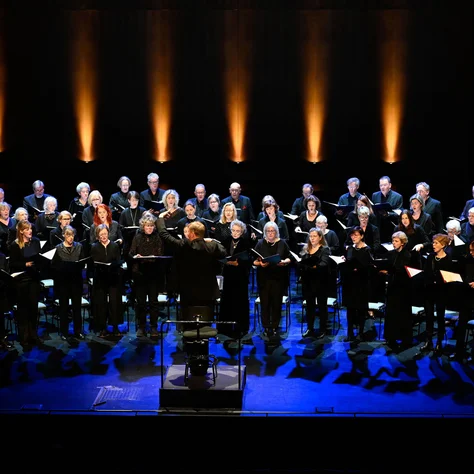 Ein großer Chor singt auf einer Bühne. Die Bühne ist blau und orange beleuchtet.