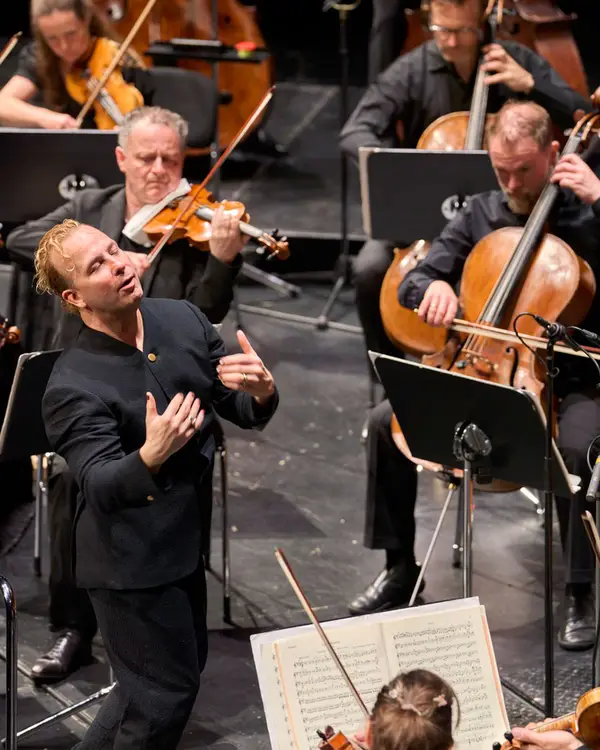 Dirigent auf der Bühne mit dem Orchester während des Konzert und fühlt die Musik mit.