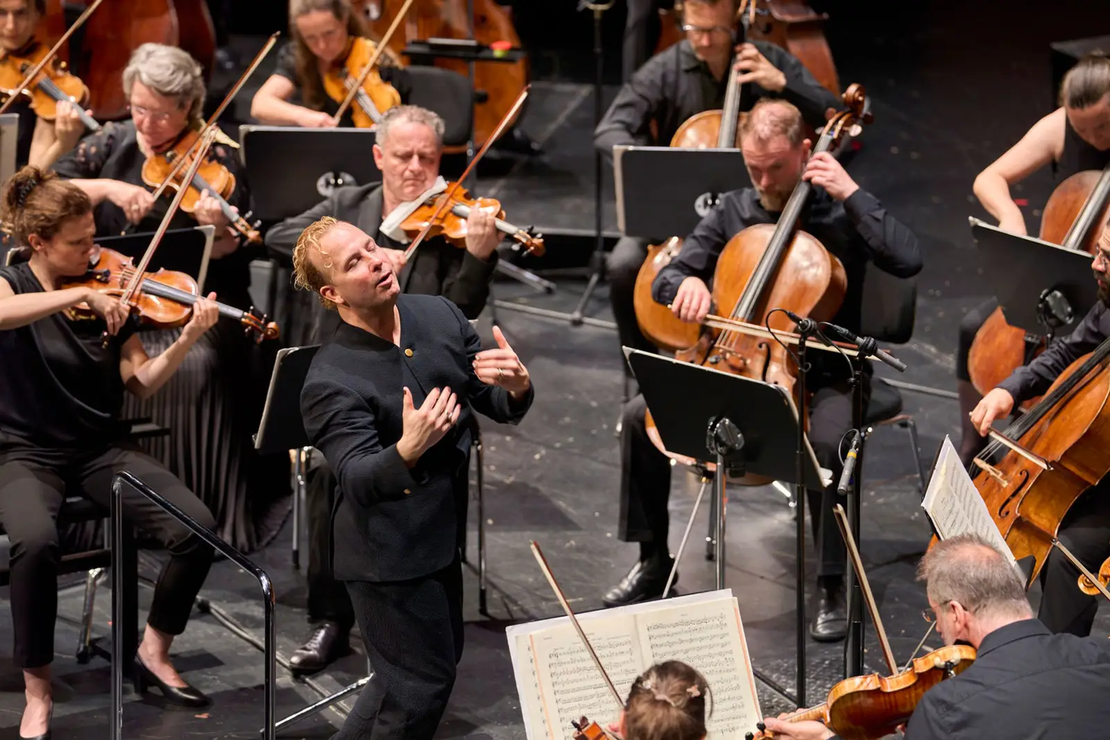 Dirigent auf der Bühne mit dem Orchester während des Konzert und fühlt die Musik mit.