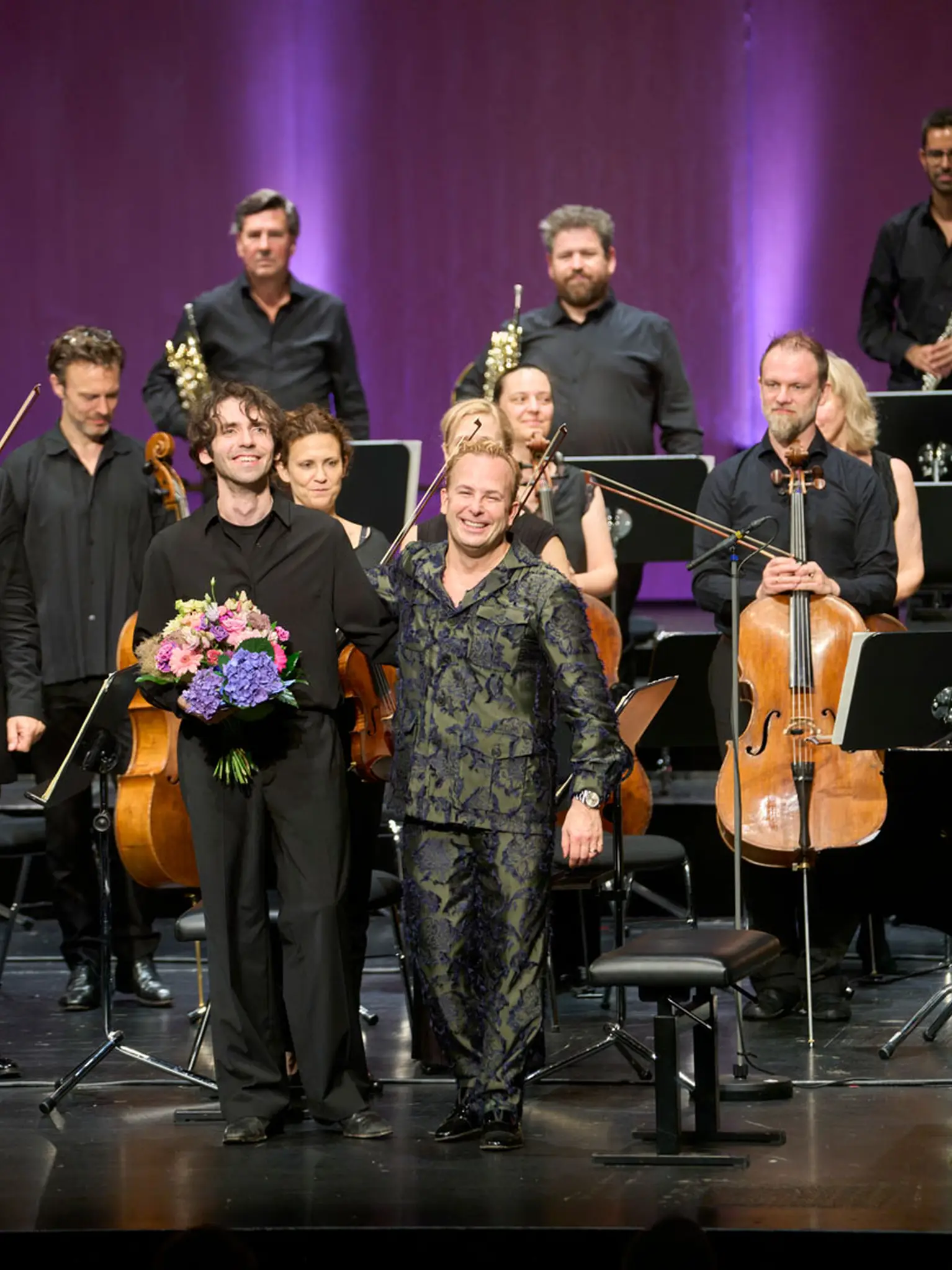 Dirigent und Pianist haben Blumensträuße in den Händen und bedanken sich herzlich beim Publikum.