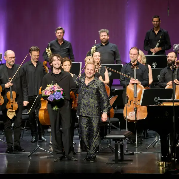 Dirigent und Pianist haben Blumensträuße in den Händen und bedanken sich herzlich beim Publikum.