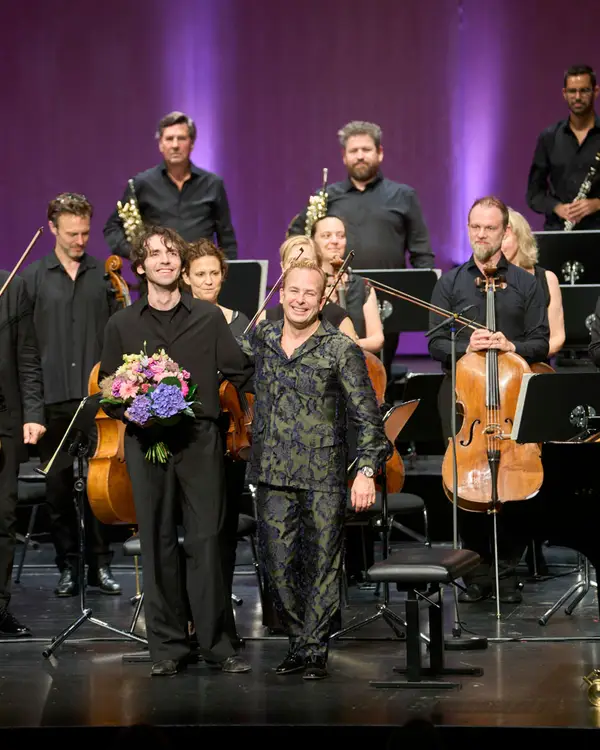 Dirigent und Pianist haben Blumensträuße in den Händen und bedanken sich herzlich beim Publikum.