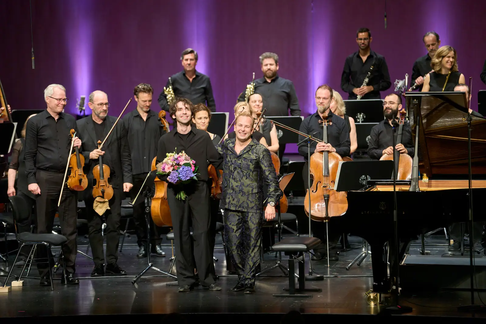 Dirigent und Pianist haben Blumensträuße in den Händen und bedanken sich herzlich beim Publikum.