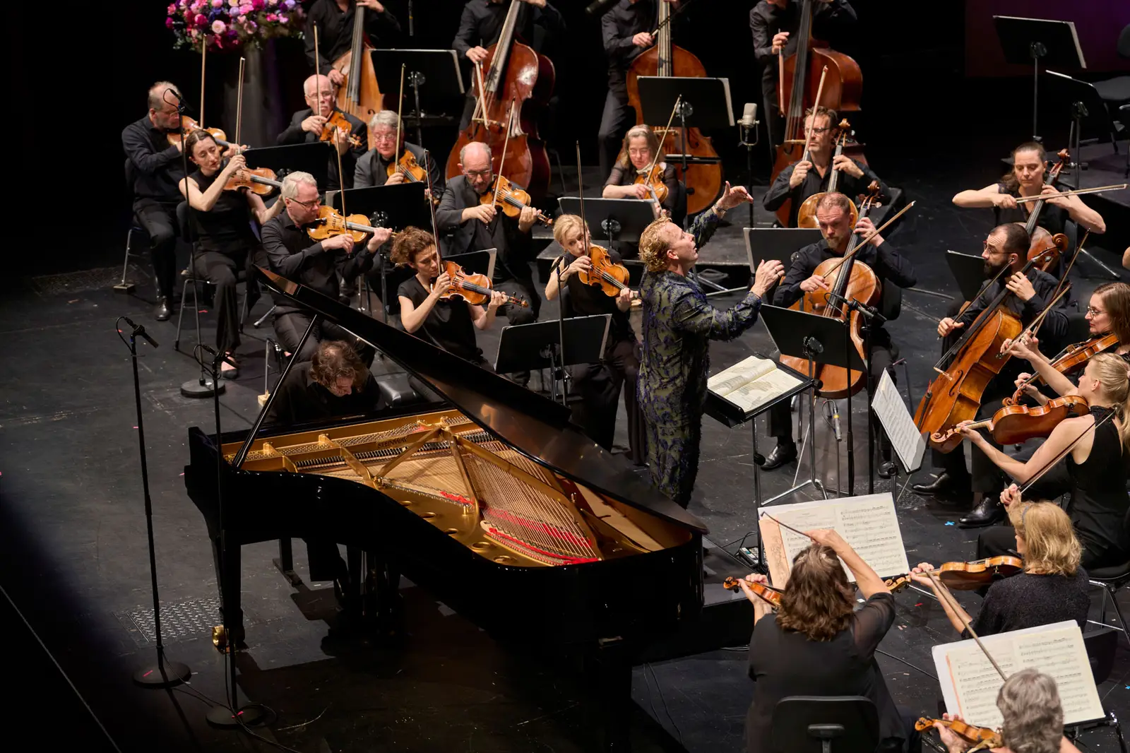 Pianist spielt am Klavier und Dirigent leitet das Orchester während dem Konzert.