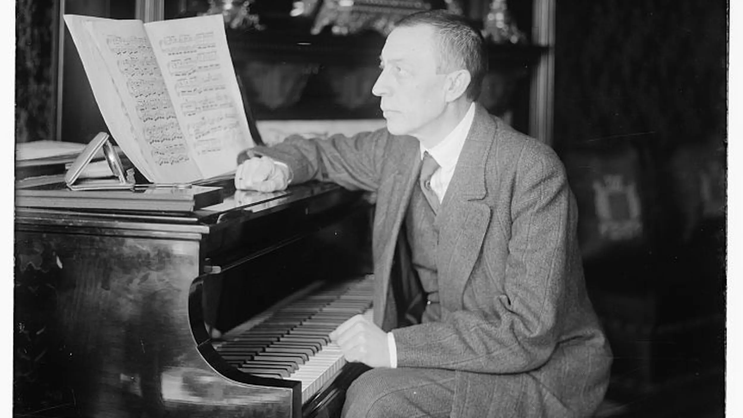 Schwarz-weiß Fotografie von Sergei Rachmaninow. Er sitzt am Klavier und blickt auf die Noten