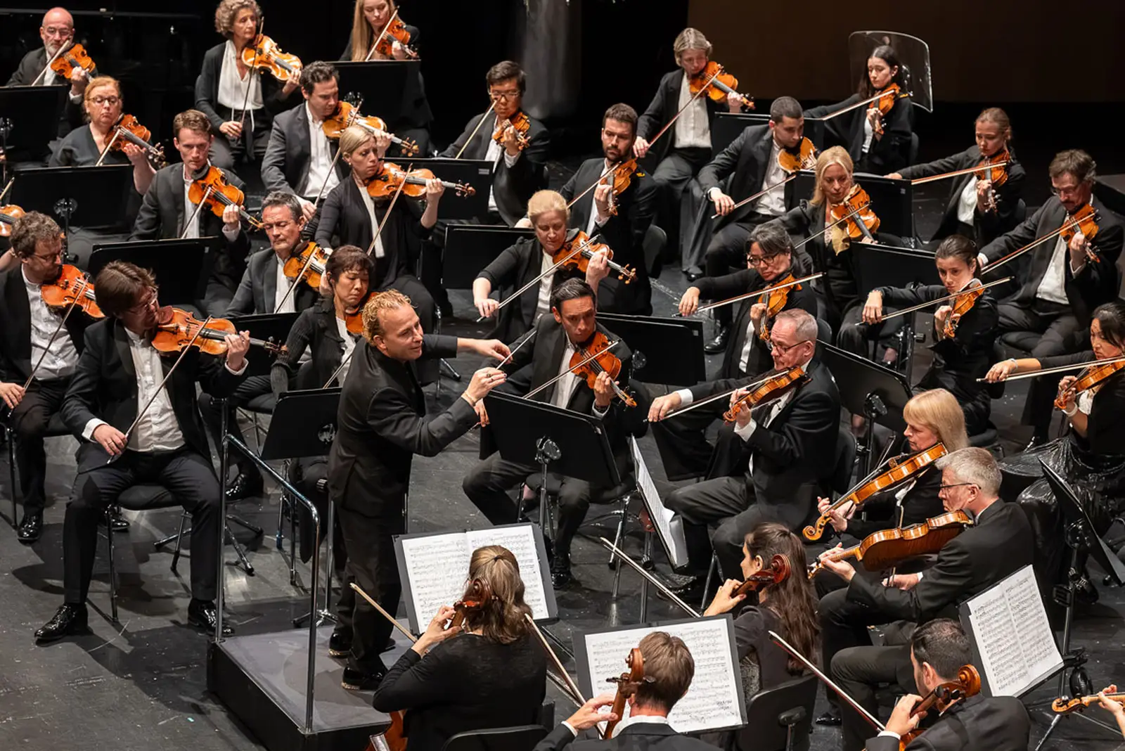 Ein Dirigent steht mit seinem Orchester auf einer großen Bühne.