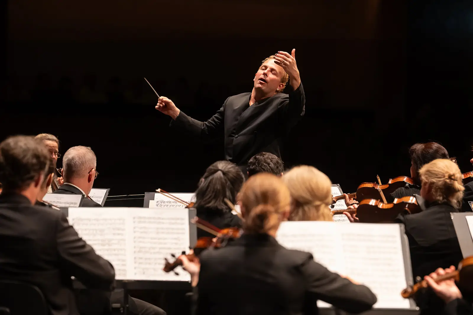 Ein Dirigent steht vor dem Orchester und dirigiert es mit viel Gefühl.