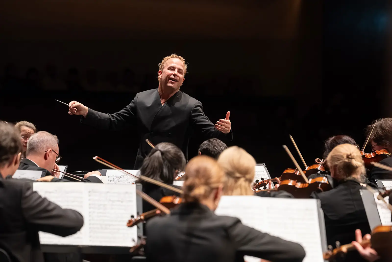 Ein Dirigent steht vor dem Orchester und dirigiert das mit viel Gefühl.