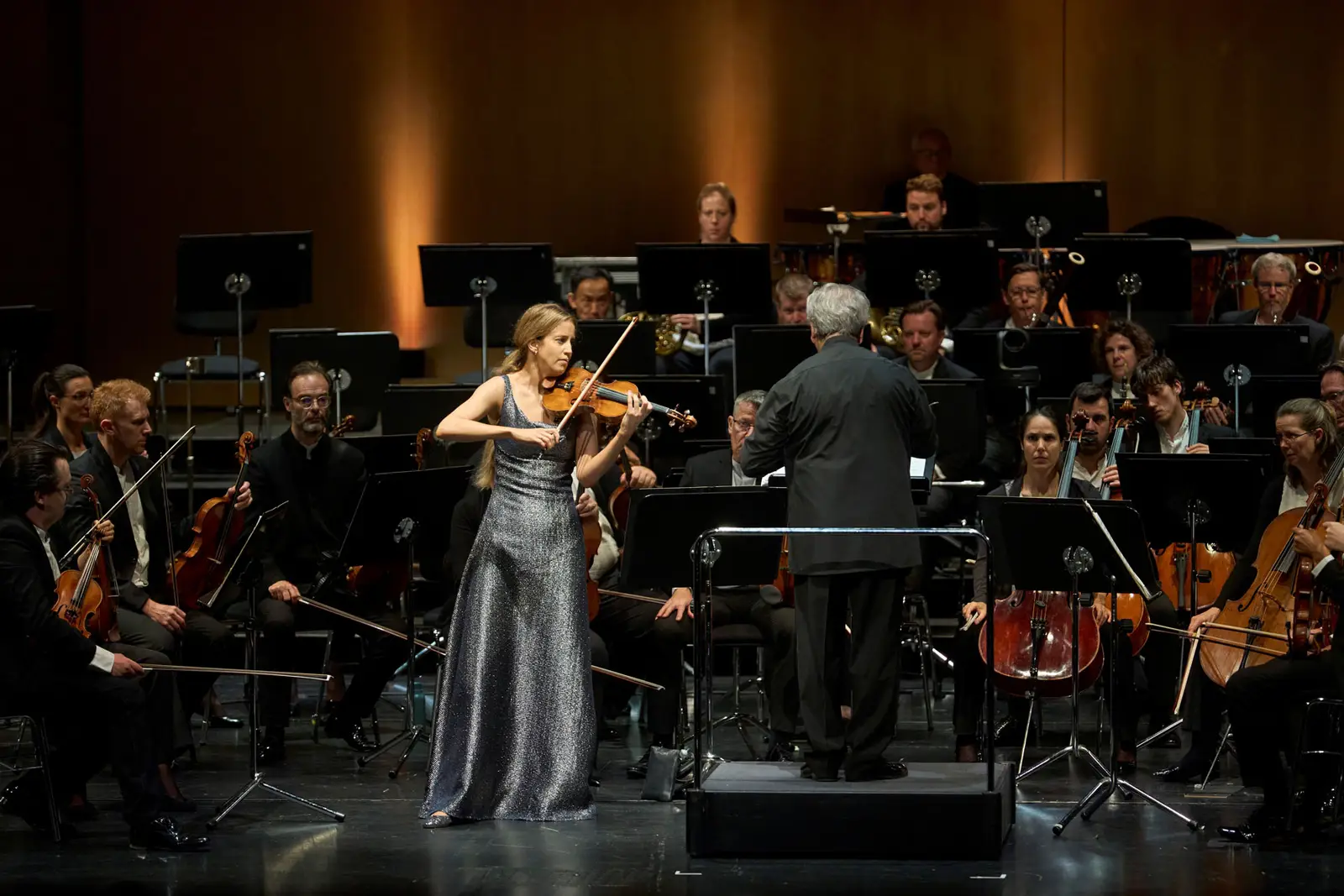 Eine Violinistin spielt gemeinsam mit einem Orchester. Sie blickt zum Dirigenten, der dem Orchester zugewandt ist.