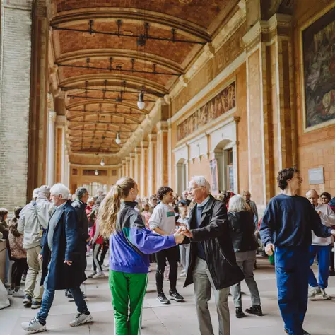 Des personnes dansent et interagissent dans une grande salle historique, avec des plafonds voûtés et des murs décorés, créant une ambiance animée.