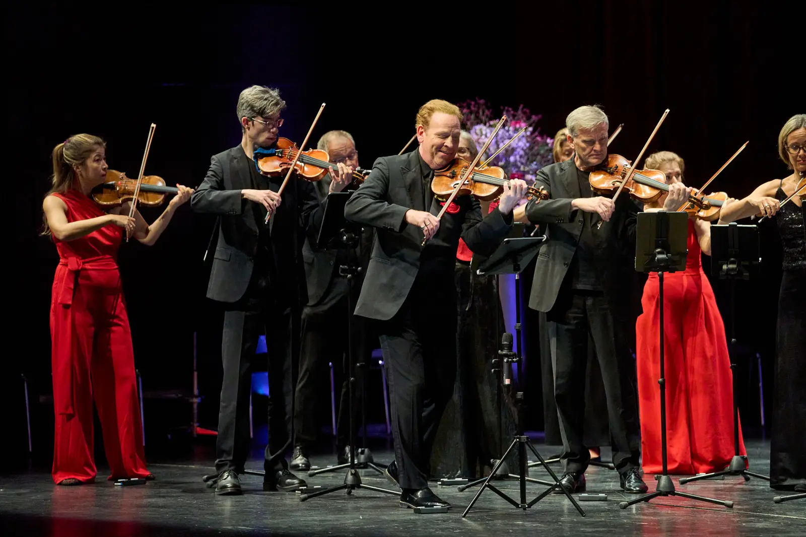 Die Violinisten eines Orchesters spielen gemeinsam auf einer Bühne.