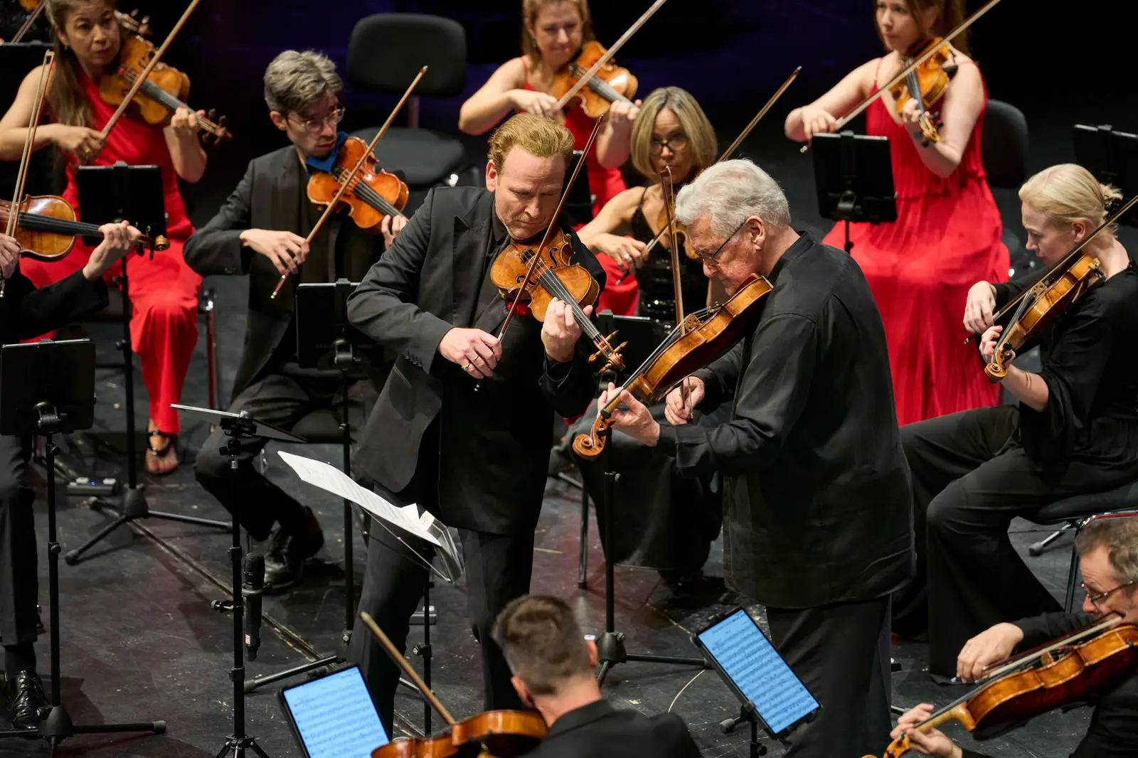 Nahe Aufnahme eines Orchesters auf einer Bühne. Im Fokus stehen zwei Violinisten.