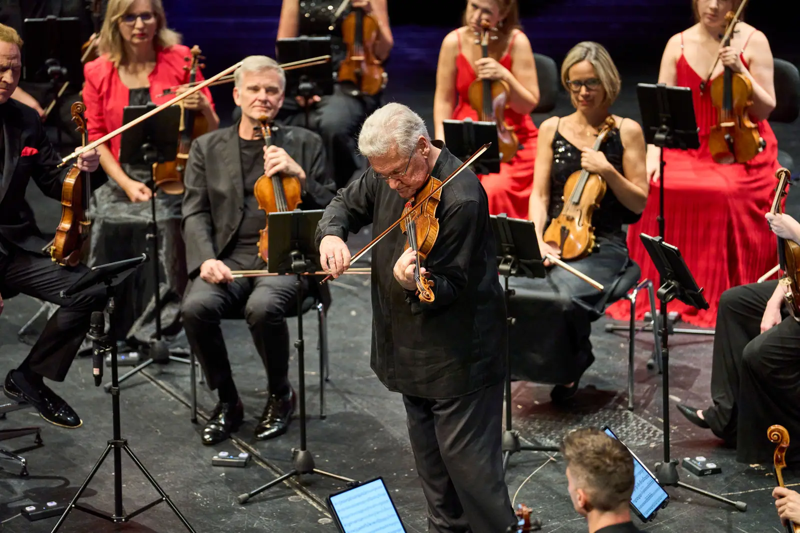 Ein Violinist steht im Vordergrund und spielt ein Solo, im Hintergrund ist das Orchester zu sehen.