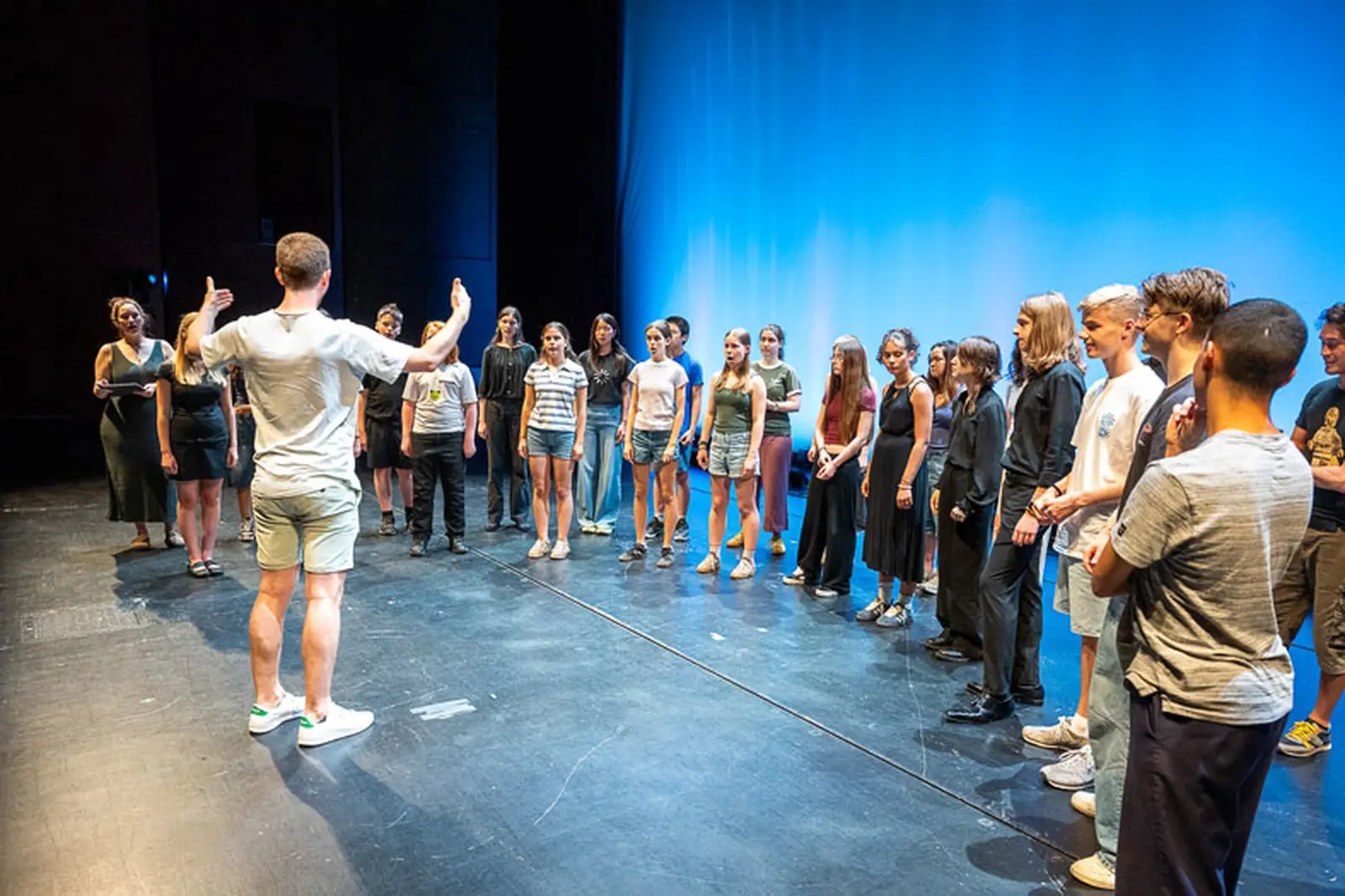 Dirigent dirigiert Kinder des Projekts auf der Bühne als Übung vor dem Konzert.