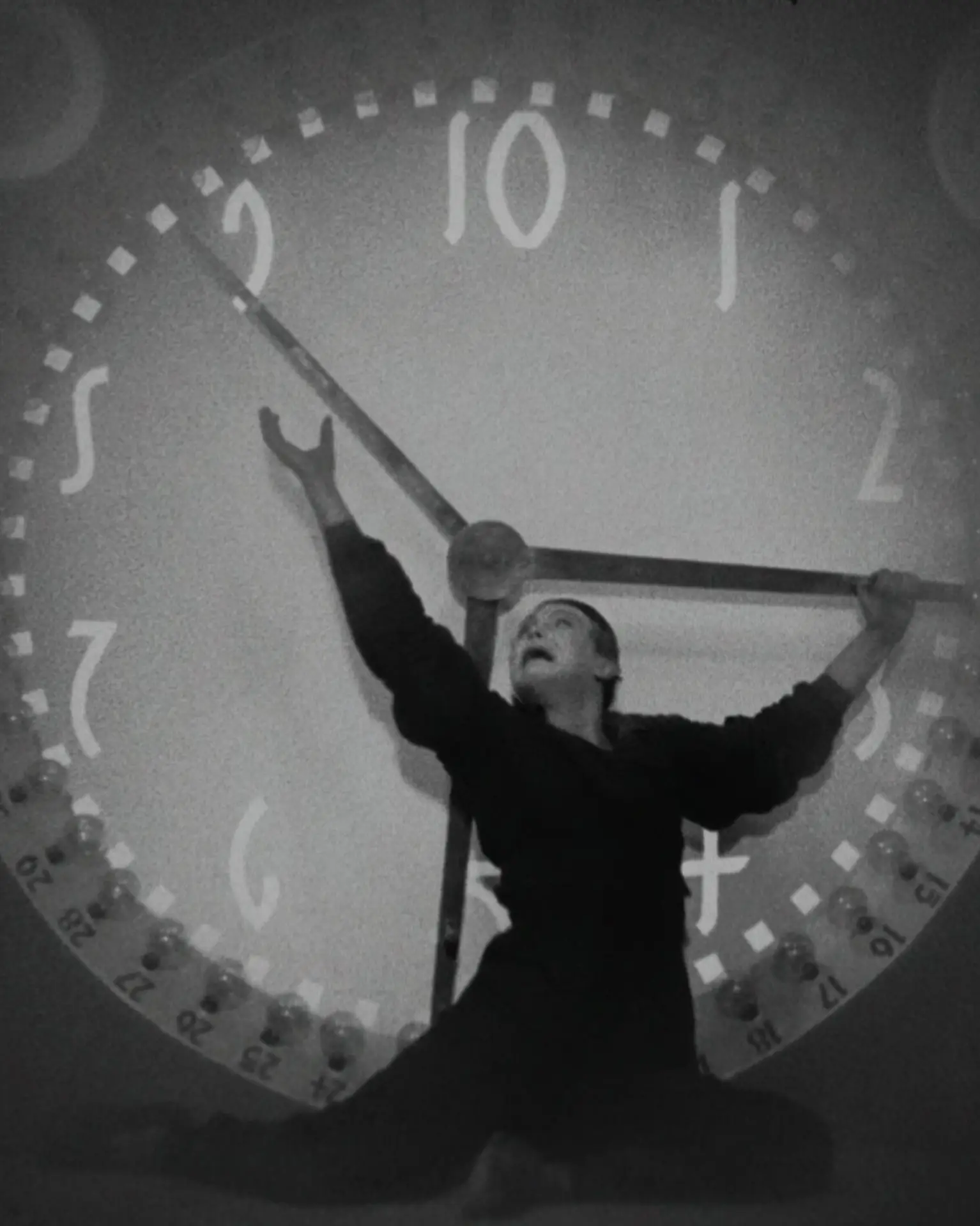 Ein Mann steht vor einer überdimensionalen Uhr und versucht die Zeiger anzuhalten.