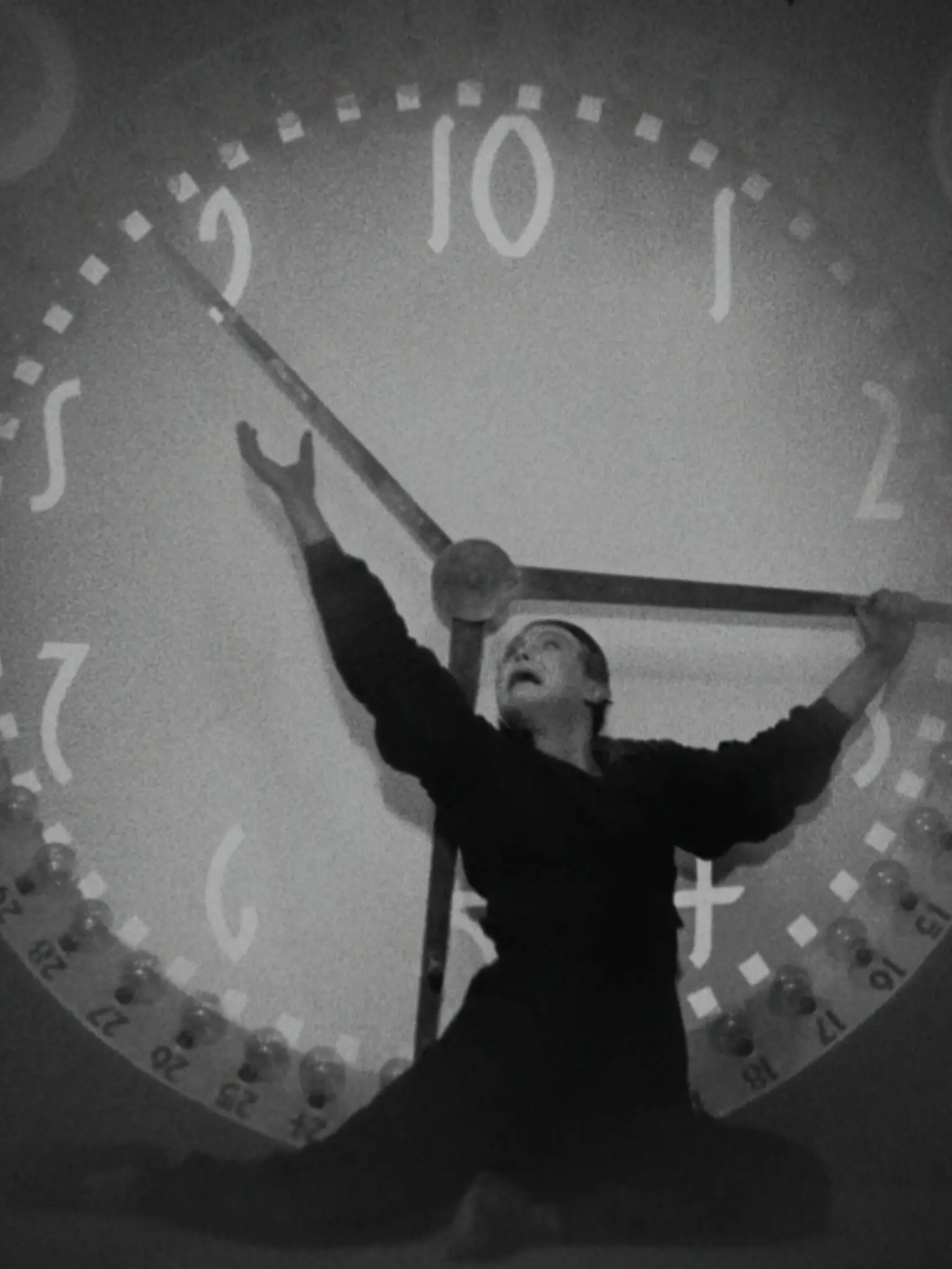 Ein Mann steht vor einer überdimensionalen Uhr und versucht die Zeiger anzuhalten.