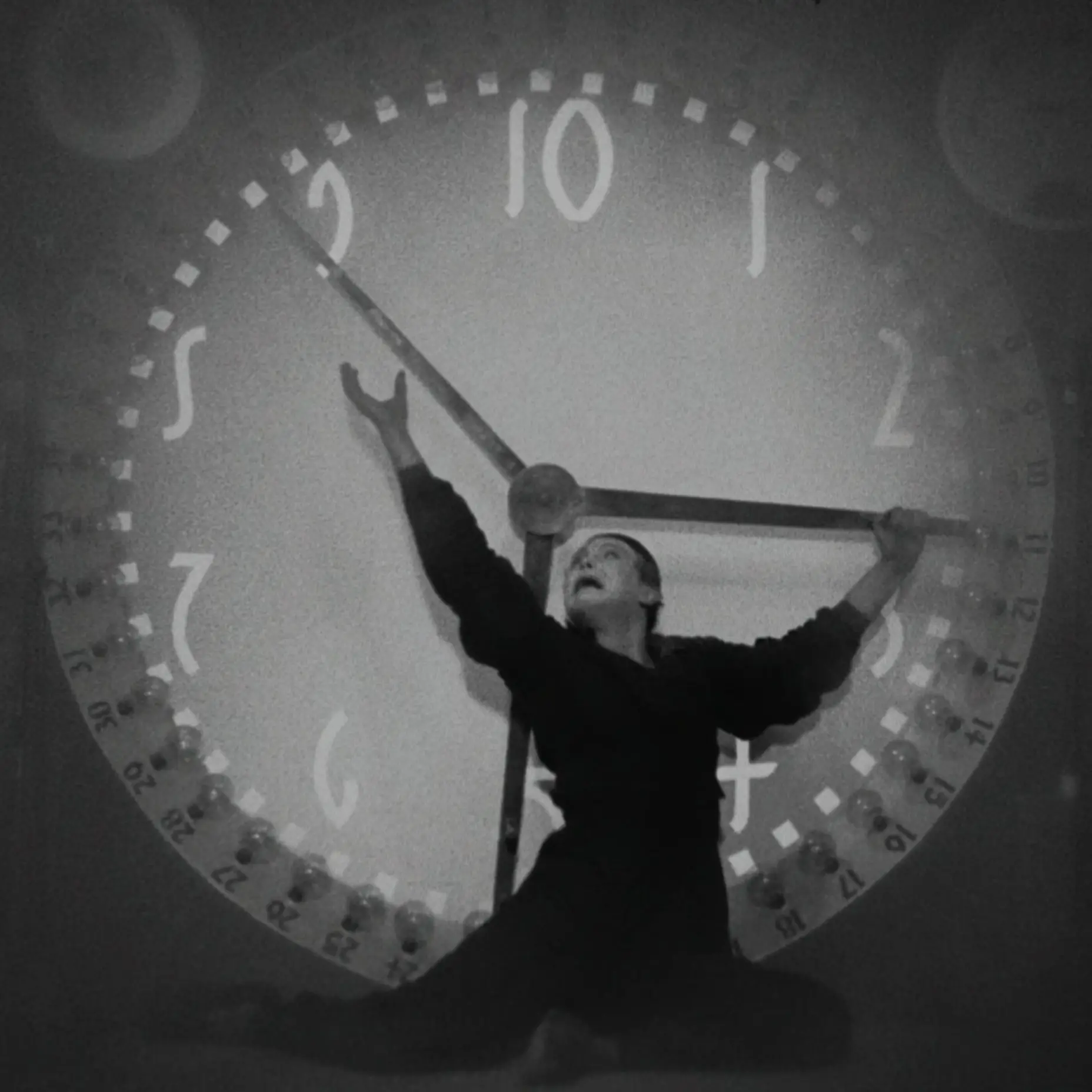 Ein Mann steht vor einer überdimensionalen Uhr und versucht die Zeiger anzuhalten.