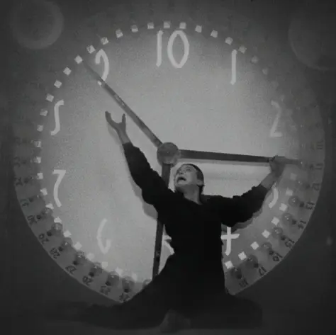 Ein Mann steht vor einer überdimensionalen Uhr und versucht die Zeiger anzuhalten.