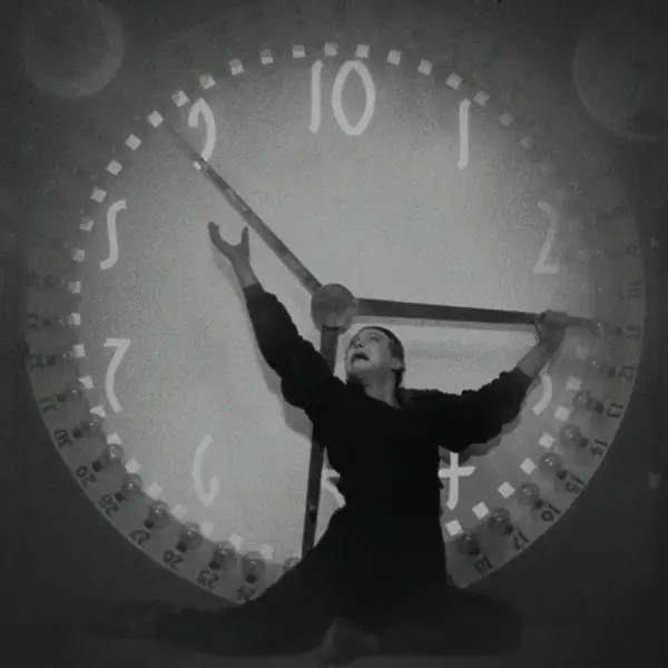 Ein Mann steht vor einer überdimensionalen Uhr und versucht die Zeiger anzuhalten.