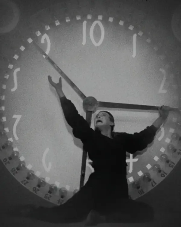 Ein Mann steht vor einer überdimensionalen Uhr und versucht die Zeiger anzuhalten.