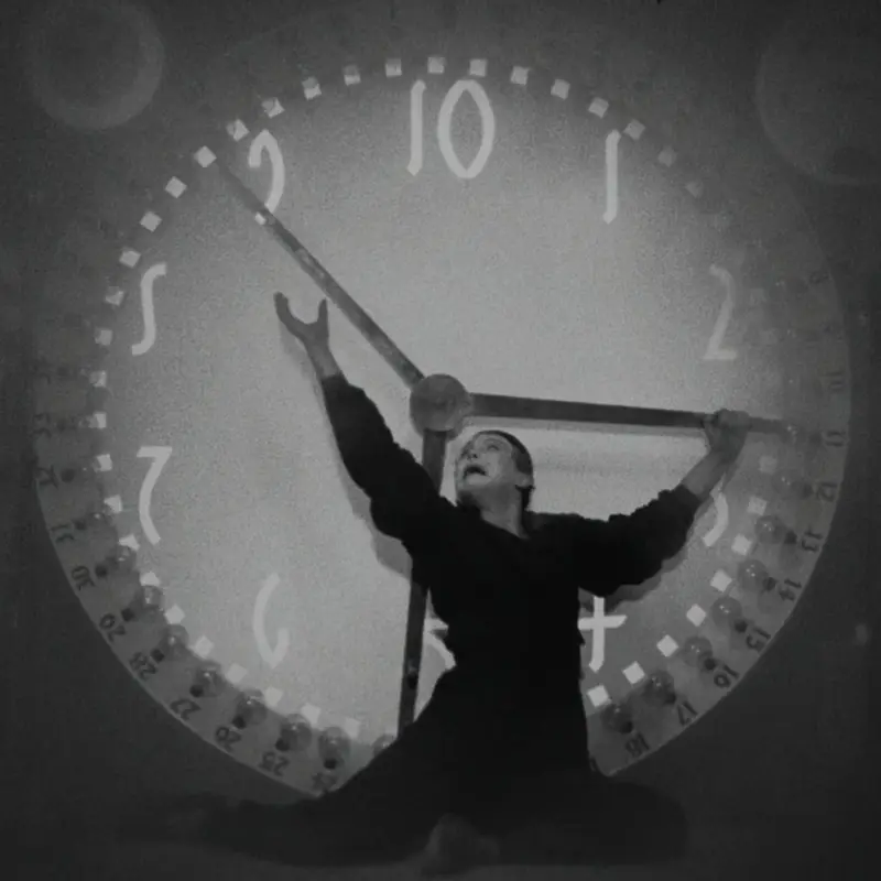 Ein Mann steht vor einer überdimensionalen Uhr und versucht die Zeiger anzuhalten.