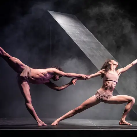 Man sieht zwei Balletttänzer auf der Bühne. Sie heben sich aneinander fest und machen große Bewegungen. Beide tragen hautfarbene Kleidung.