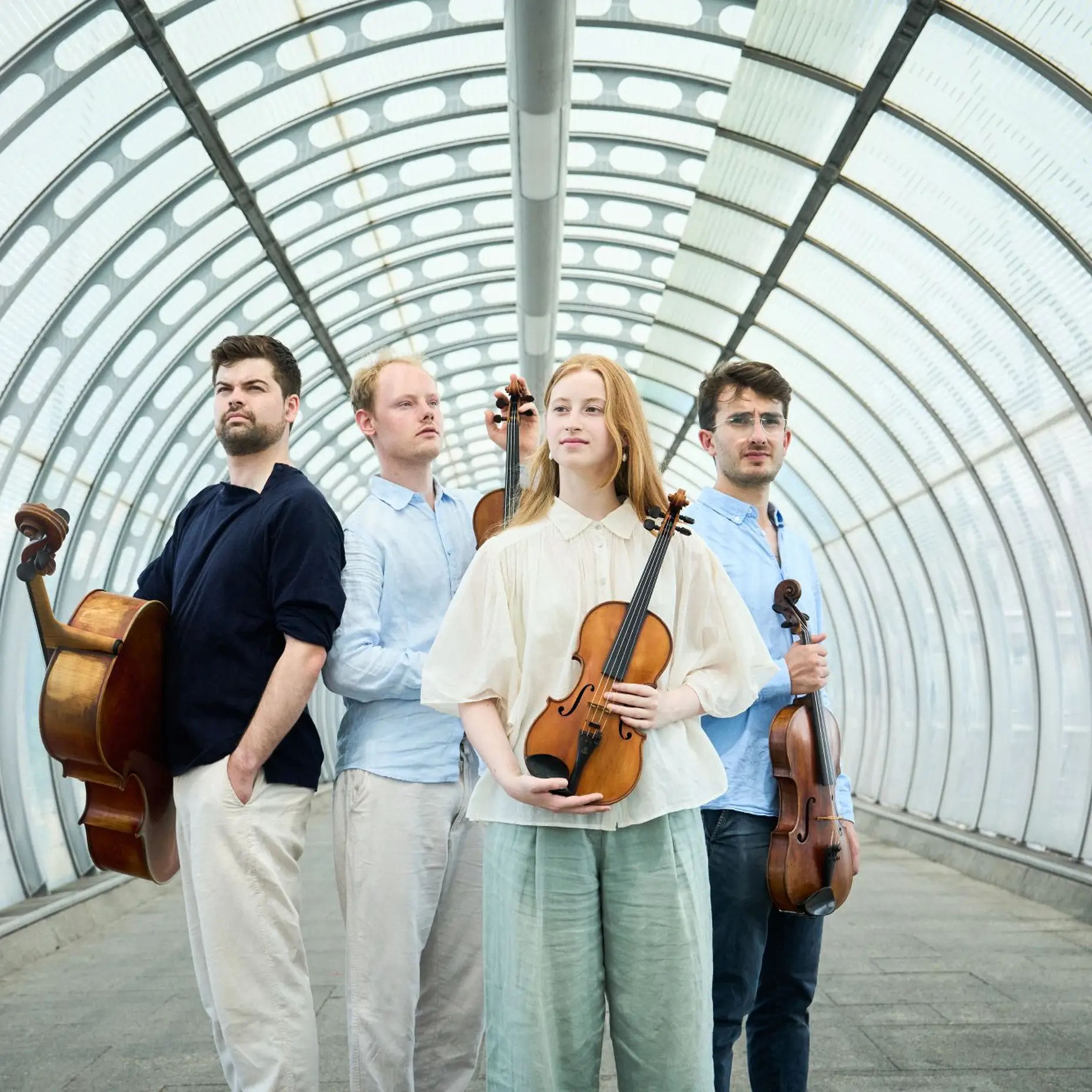 Es stehen vier Erwachsene in einem hellen Durchgang und jeder hält ein Streichinstrument in der Hand. Es sind drei Männer und eine Frau. Alle sind elegant, legere gekleidet.