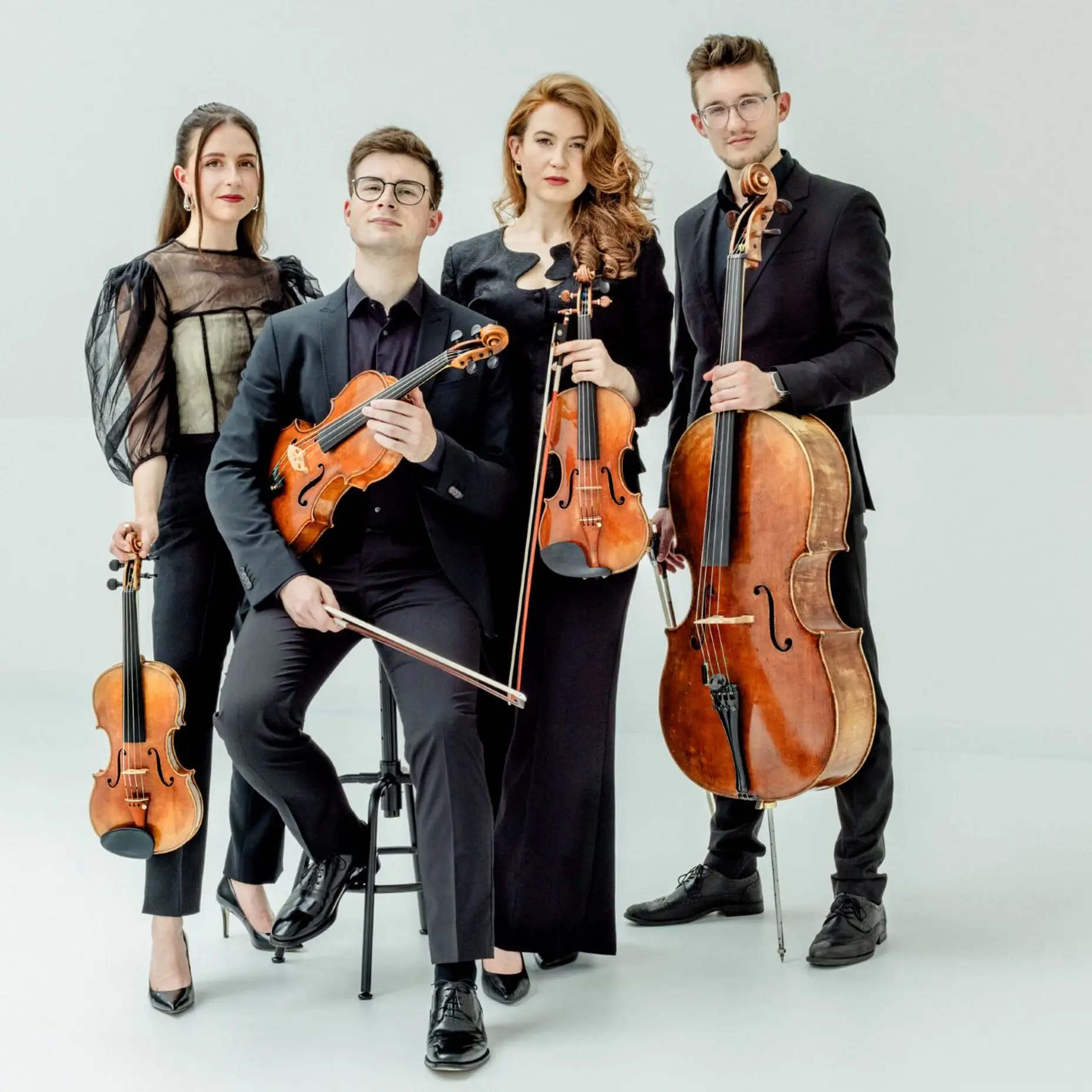 Zwei Frauen und zwei Männer stehen mit Streichinstrumenten in eleganter Kleidung.
