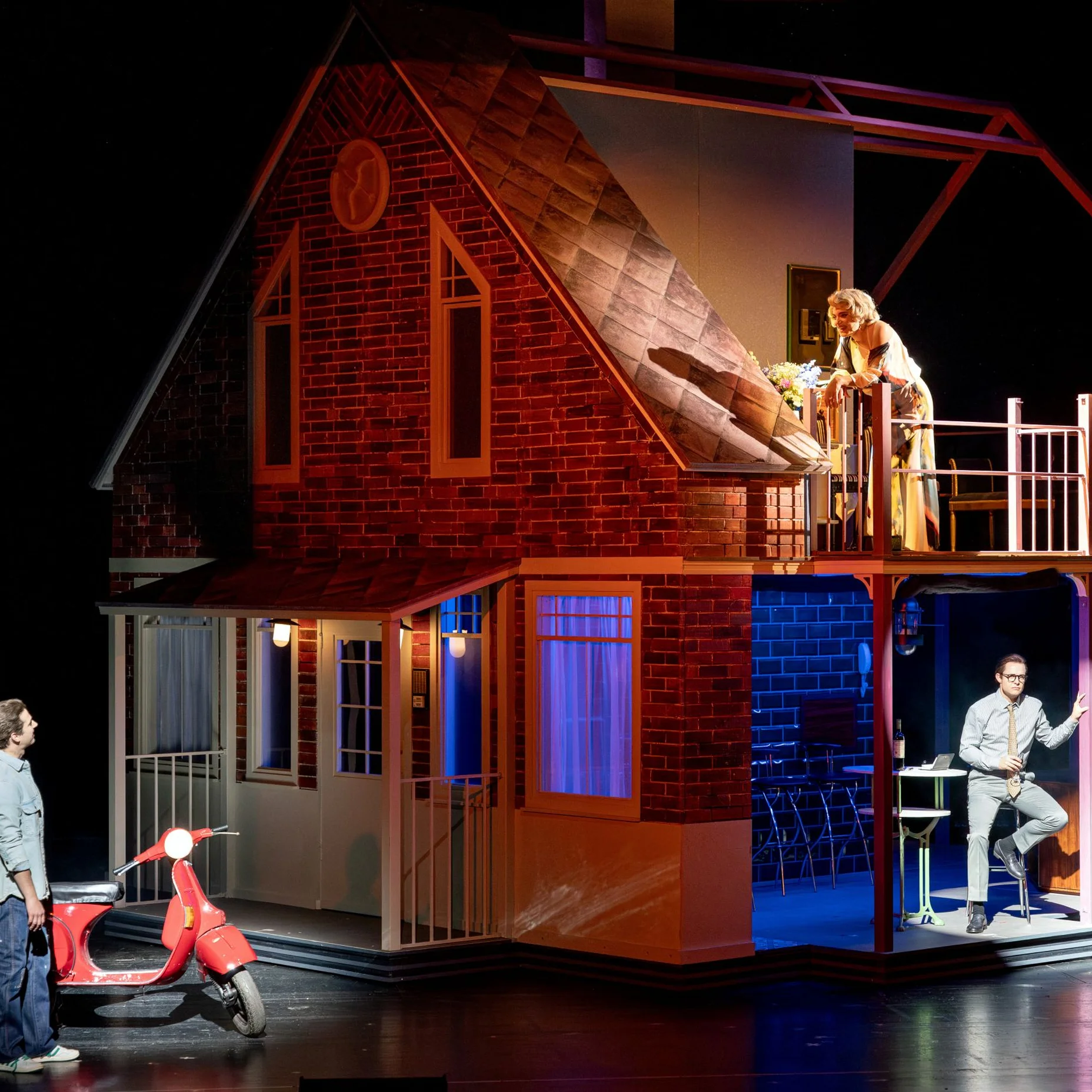 Bühnenbild des Musical "Hello Again" mit einem zweistöckigen Haus. Charaktere interagieren, eine Person steht unten, eine oben auf dem Balkon.