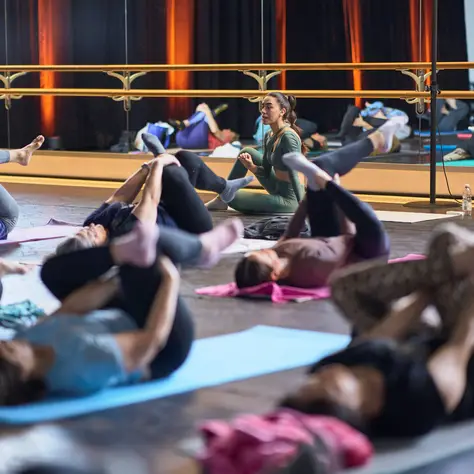 Eine Gruppe von Menschen praktiziert Yoga in einem Studio. Alle liegen auf Matten und machen Stretching-Übungen vor einem Spiegel.