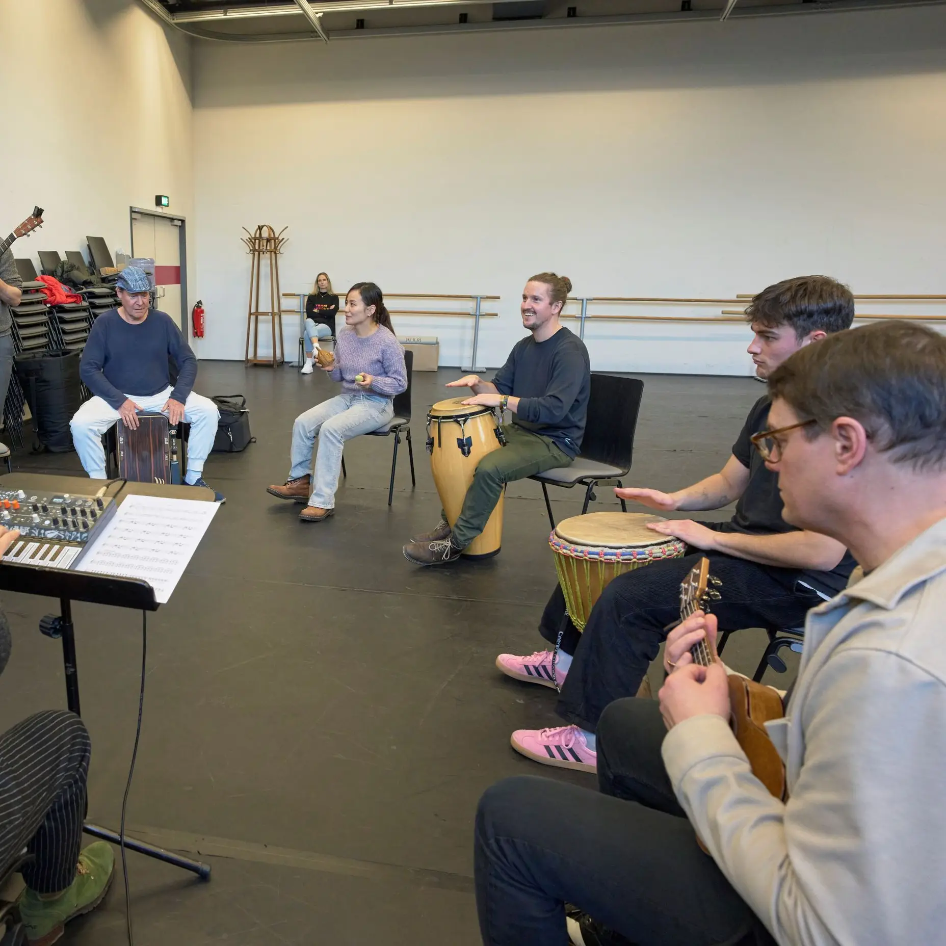 A group rehearsing in a room, with some playing instruments like guitar and drums, while another person conducts.