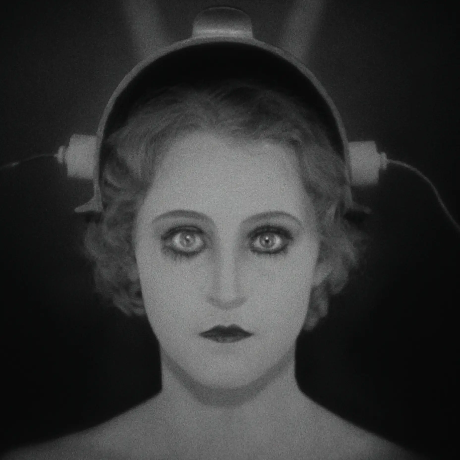 Schwarz-Weiß-Bild einer Frau mit intensiven Augen, die einen futuristischen Helm trägt. Der Hintergrund ist dunkel gehalten.