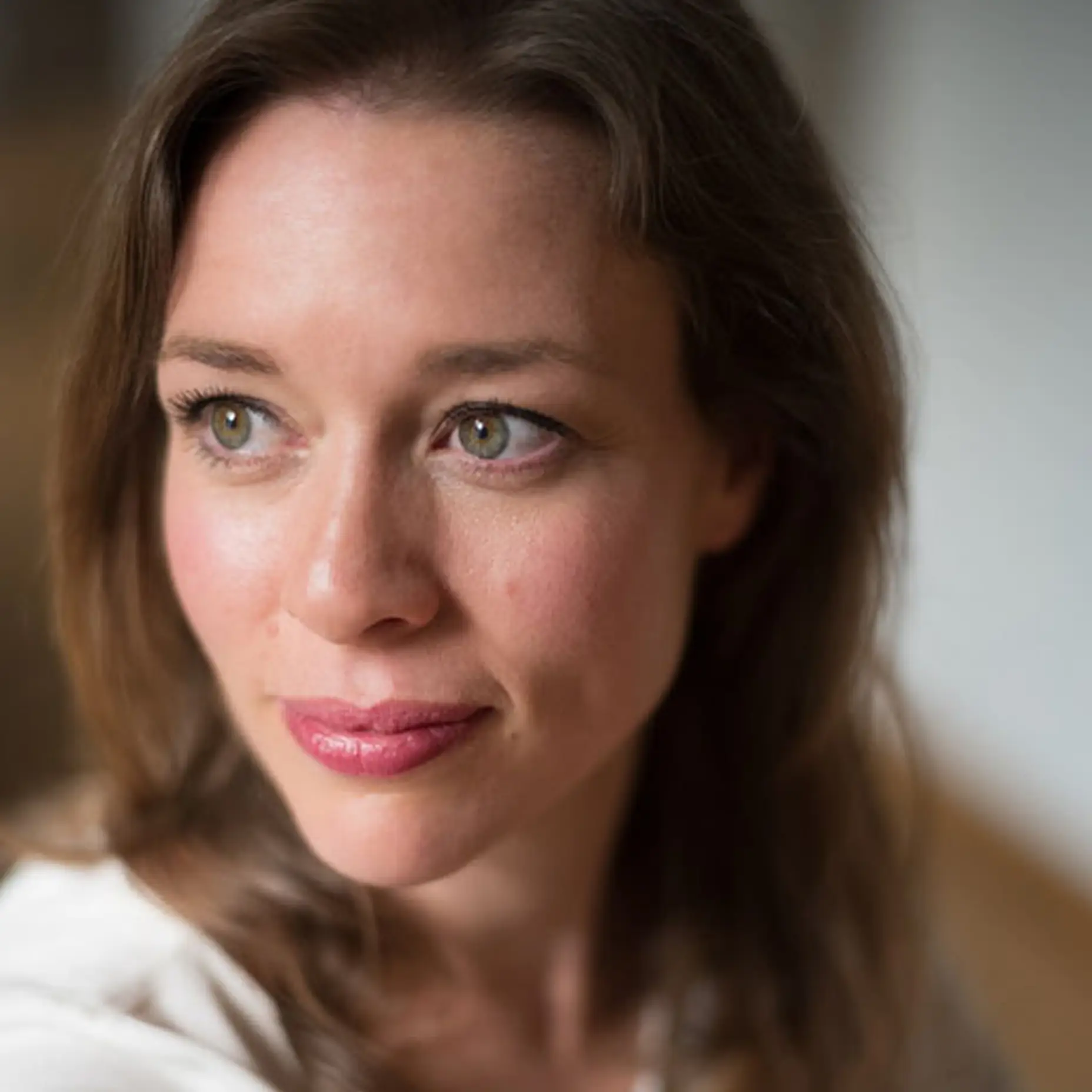 Porträt einer Frau mit braunem Haar, in einem weißen Oberteil. Sie blickt nach rechts, mit natürlichem Licht.