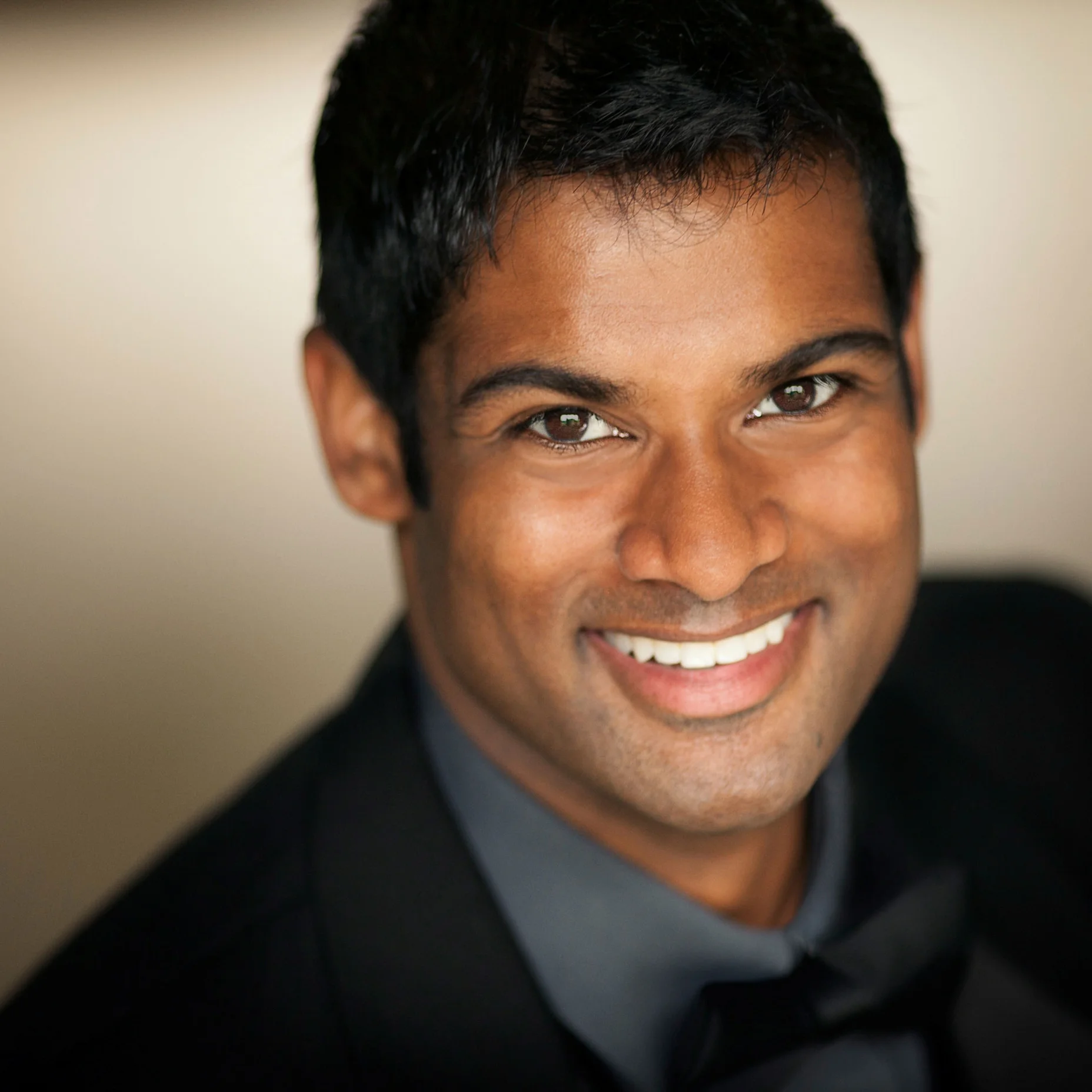 Sean Panikkar trägt einen dunklen Anzug und lächelt freundlich in die Kamera. Der Hintergrund ist leicht verschwommen.