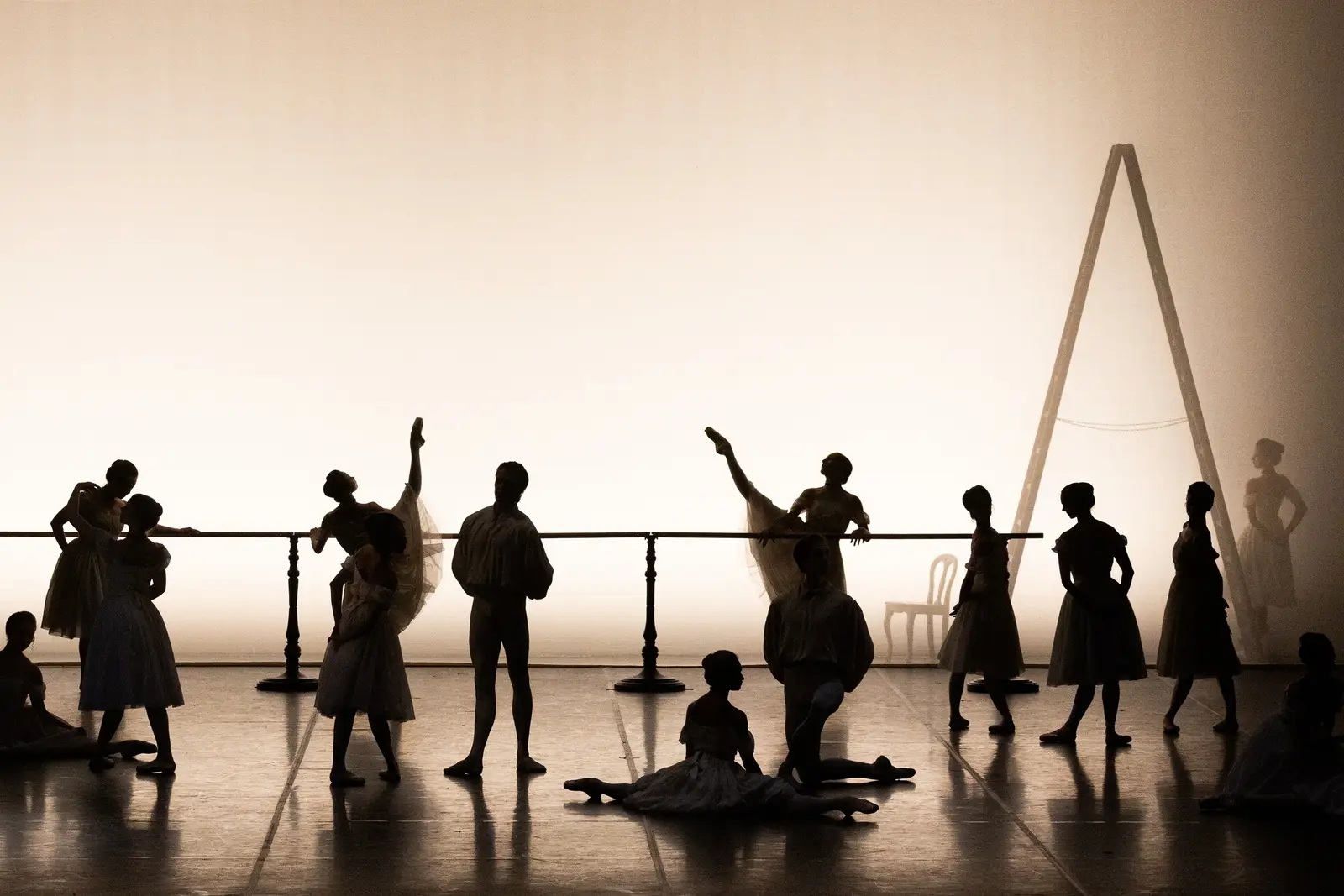 Silhouetten von Tänzern proben an einer Ballettstange auf einer Bühne. Die Beleuchtung schafft eine dramatische Atmosphäre.