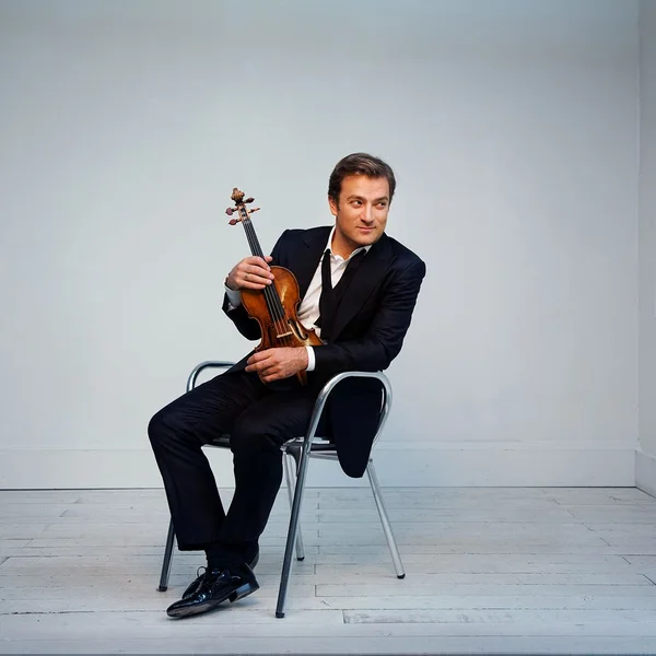 Renaud Capucon sitzt auf einem Stuhl in einem modernen Raum und hält eine Geige. Er trägt einen eleganten Anzug.