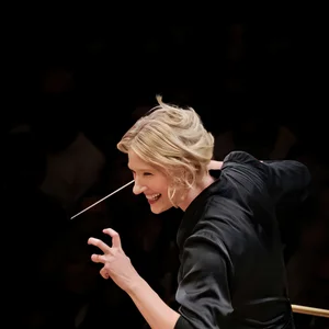 Die Dirigentin Joana Mallwitz mit kurzen, blonden Haaren dirigiert leidenschaftlich ein Orchester mit einem Taktstock in der Hand.