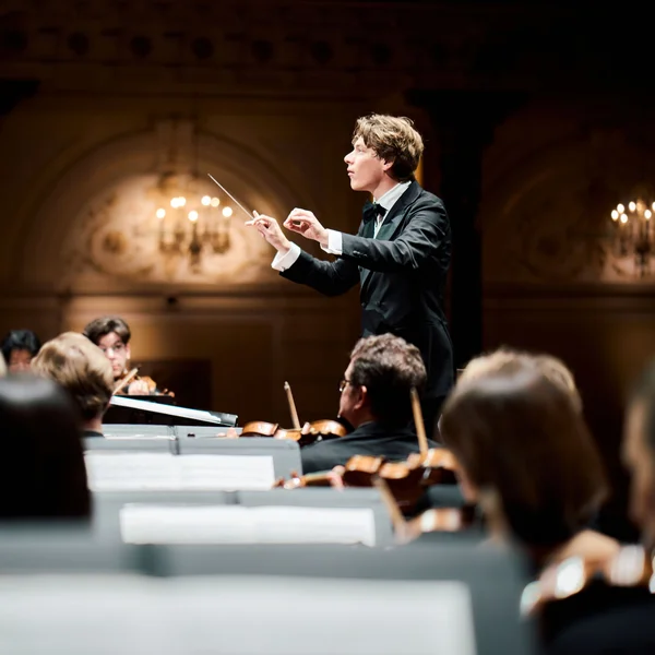 Der Dirigent Klaus Mäkelä & das Royal Concertgebouw Orchestra leitet das Royal Concertgebouw Orchestra während eines Auftritts. Musiker sind mit Instrumenten zu sehen, die Bühne ist elegant beleuchtet.