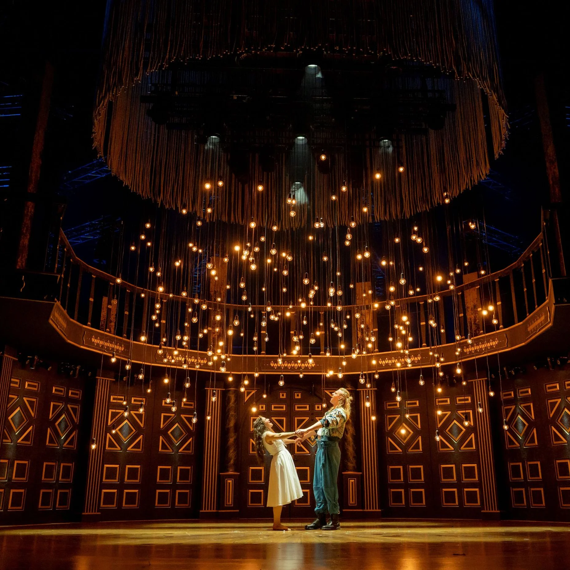 Die Theaterbühne von Romeo & Julia mit aufwendigem Holzhintergrund und unzähligen Lichtern. Zwei Darsteller stehen in eleganter Pose im Mittelpunkt.