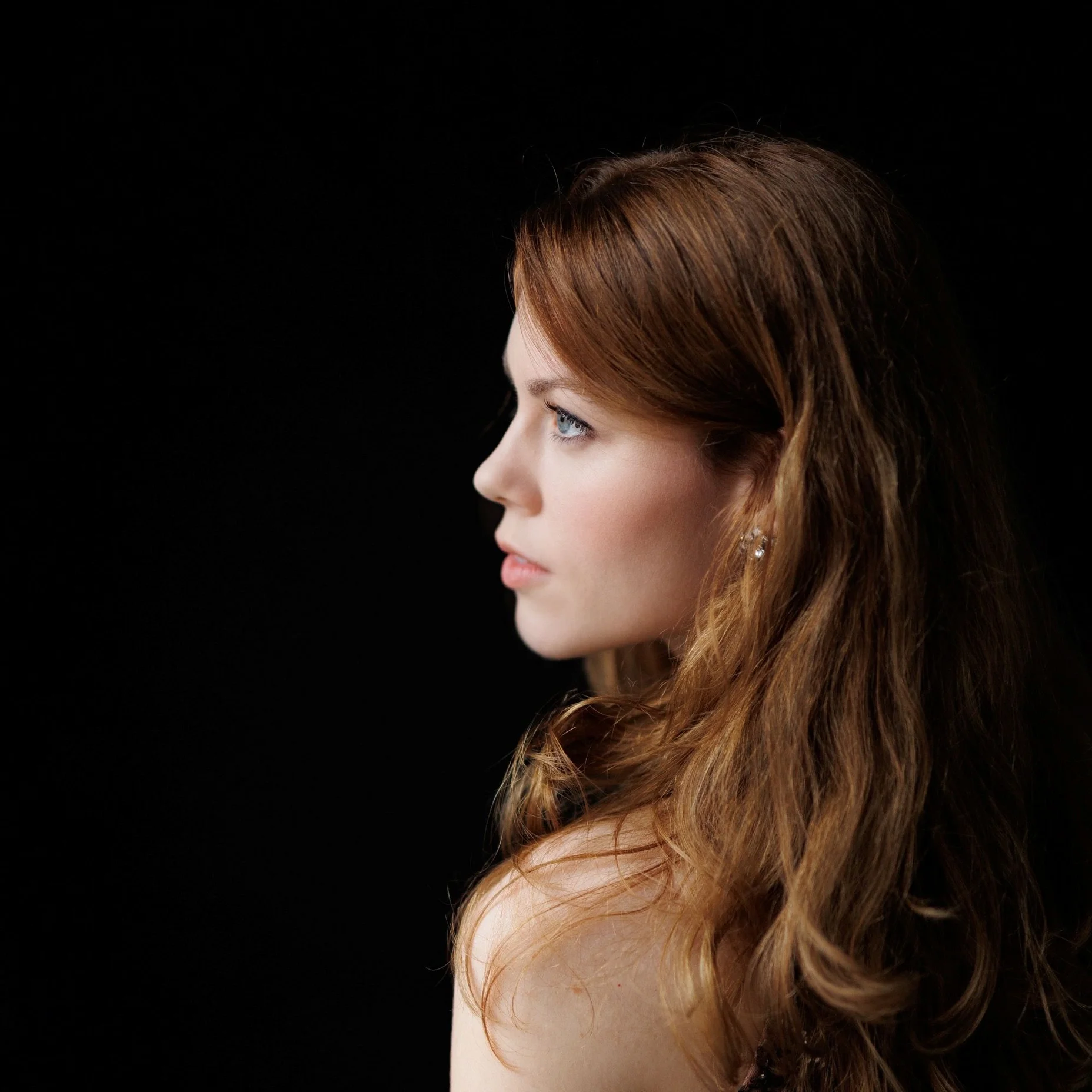 Samantha Gaul mit langen, welligen Haaren, die zur Seite schaut, vor einem schwarzen Hintergrund. Elegante und nachdenkliche Ausstrahlung.