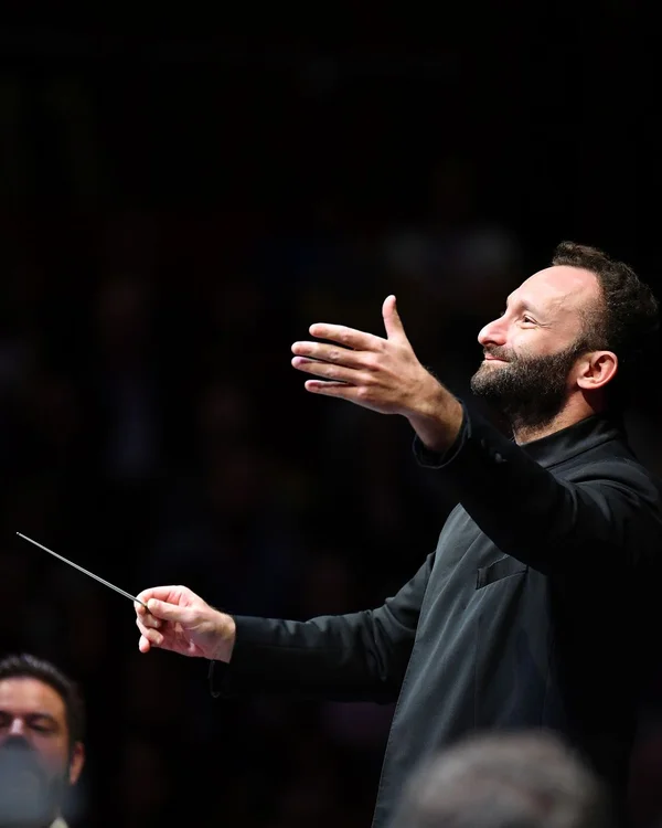 Kirill Petrenko in schwarzer Kleidung leitet mit einem Taktstock ein Orchester. Sein Gesichtsausdruck ist konzentriert und leidenschaftlich.
