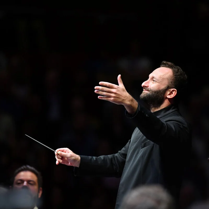 Kirill Petrenko in black attire leads an orchestra with a baton, exhibiting a focused and passionate expression.