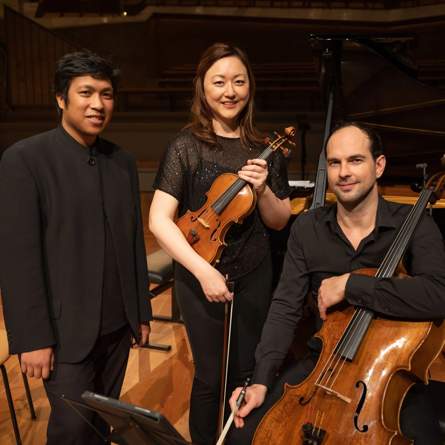 Das Pangaea Trio Berlin stehen auf einer Bühne mit ihren Instrumenten. Eine Frau hält eine Violine, daneben ein Mann mit einem Cello.