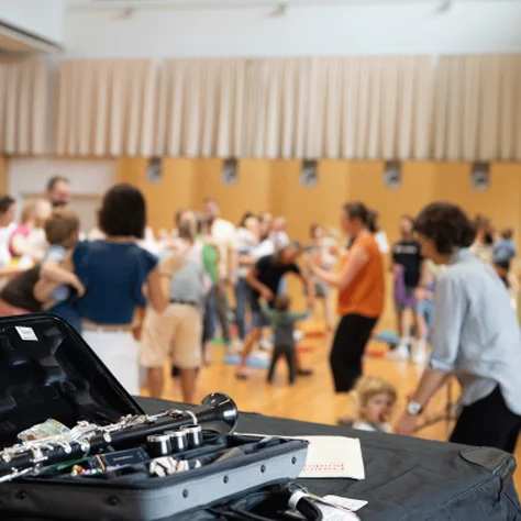 A clarinet in its case is on a table, while people in the background participate in a baby concert.