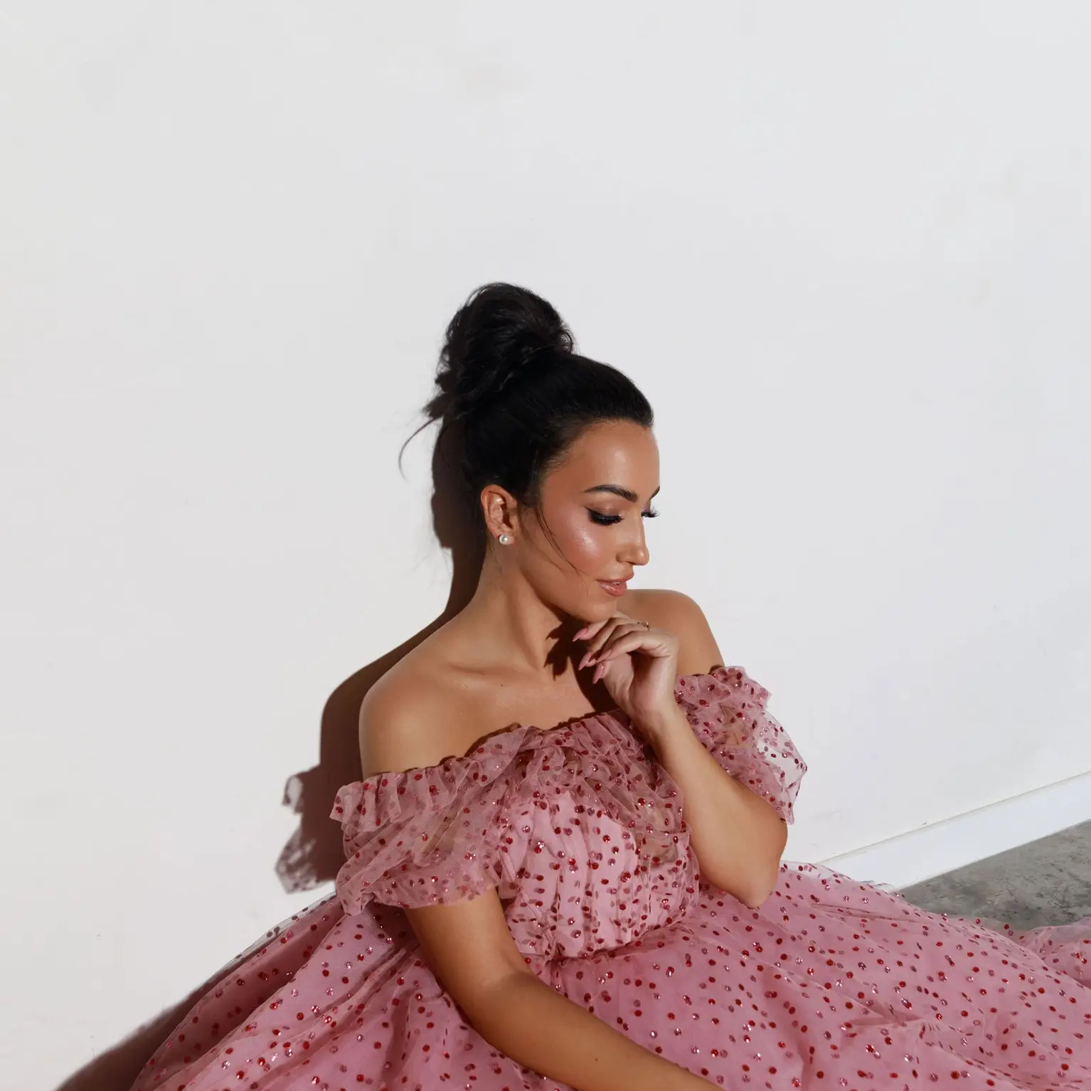 Carolina López Moreno en robe rose à sequins est assise contre un mur, regardant pensivement sur le côté.