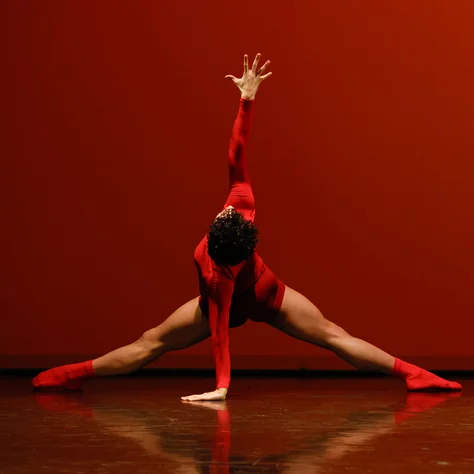 Ein Tänzer, gekleidet in Rot, führt eine ausdrucksstarke Pose auf der Bühne mit einem intensiven roten Hintergrund aus.