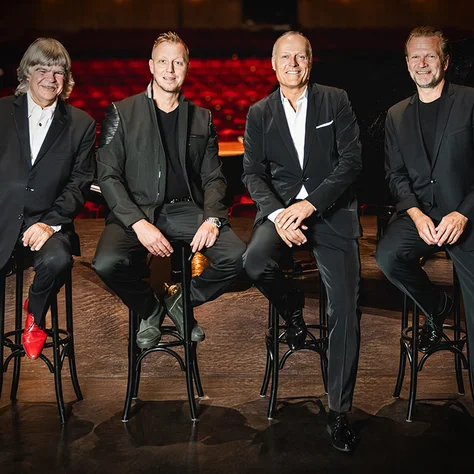 Die vier Pianisten Sebastian Knauer, Martin Tingvall, Joja Wendt and Axel Zwingenberger in black suits sit on bar stools on a stage. A piano is visible in the background.