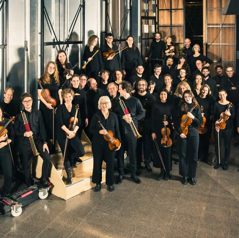 The Balthasar-Neumann-Orchestra in dark clothing stands in an industrial space with instruments, preparing for a performance.