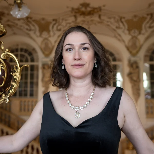 Erica Eloff in einem eleganten schwarzen Kleid steht in einem opulenten Raum mit kunstvollen goldenen Verzierungen.