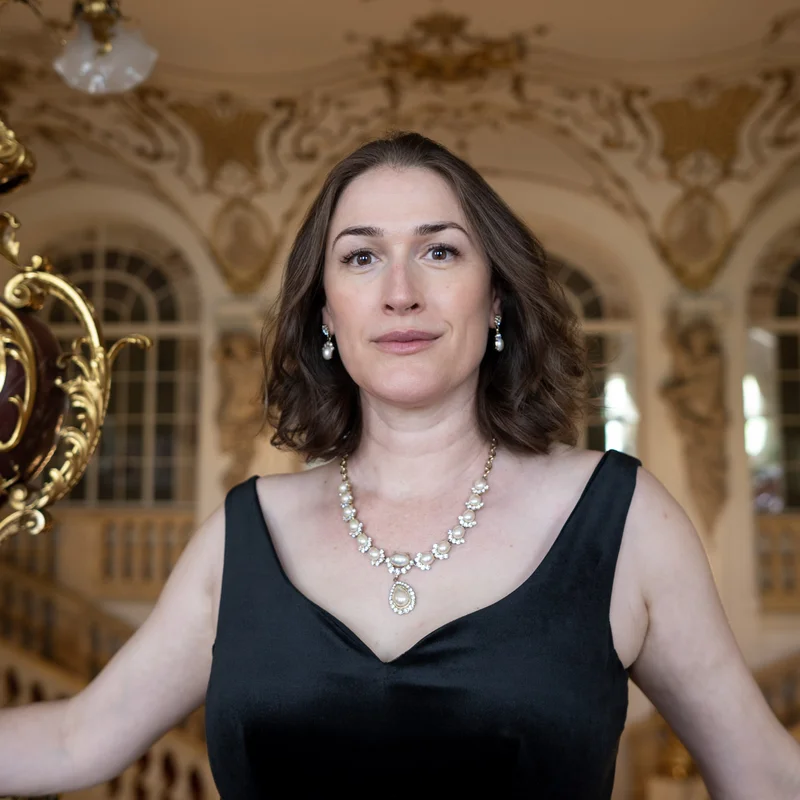 Erica Eloff in an elegant black dress stands in an opulent room adorned with intricate golden decorations.